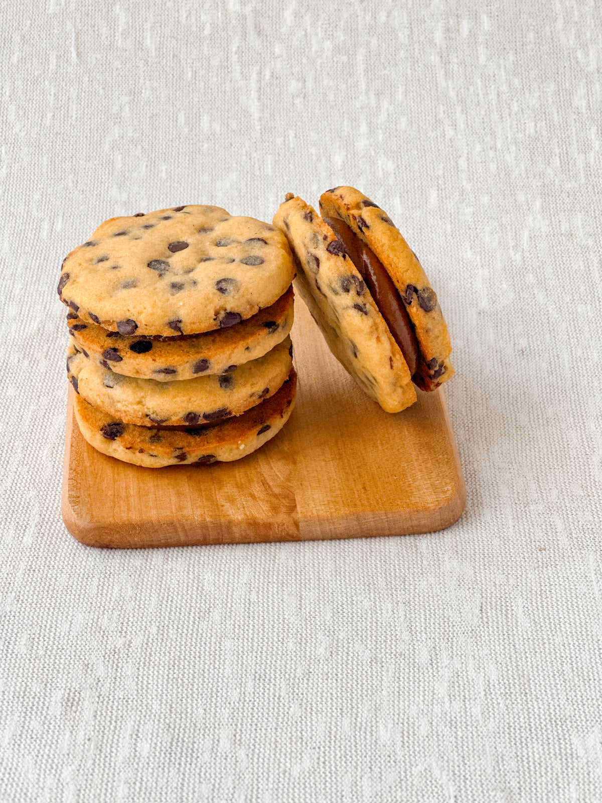 Stack of handmade alfa cookies (alfajores-style cookies) with dulce de leche, arranged on a wooden board in Perth, Australia.