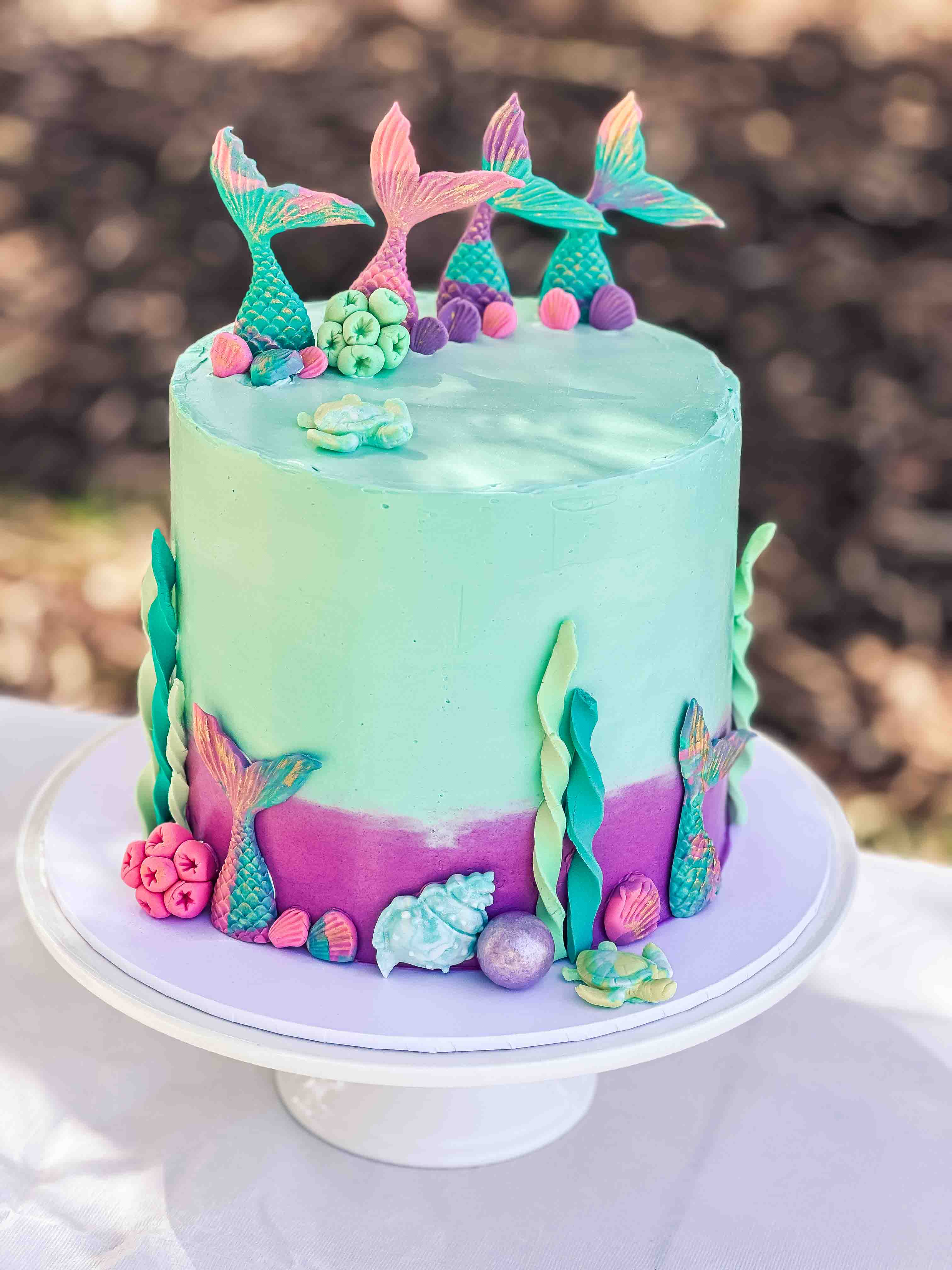 Mermaid‑themed cake with turquoise and fuchsia ocean decorations and mermaid tails on top, handmade in Perth.