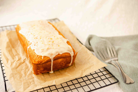 Orange loaf with white icing on a cooling rack with a fork and napkin in the background.