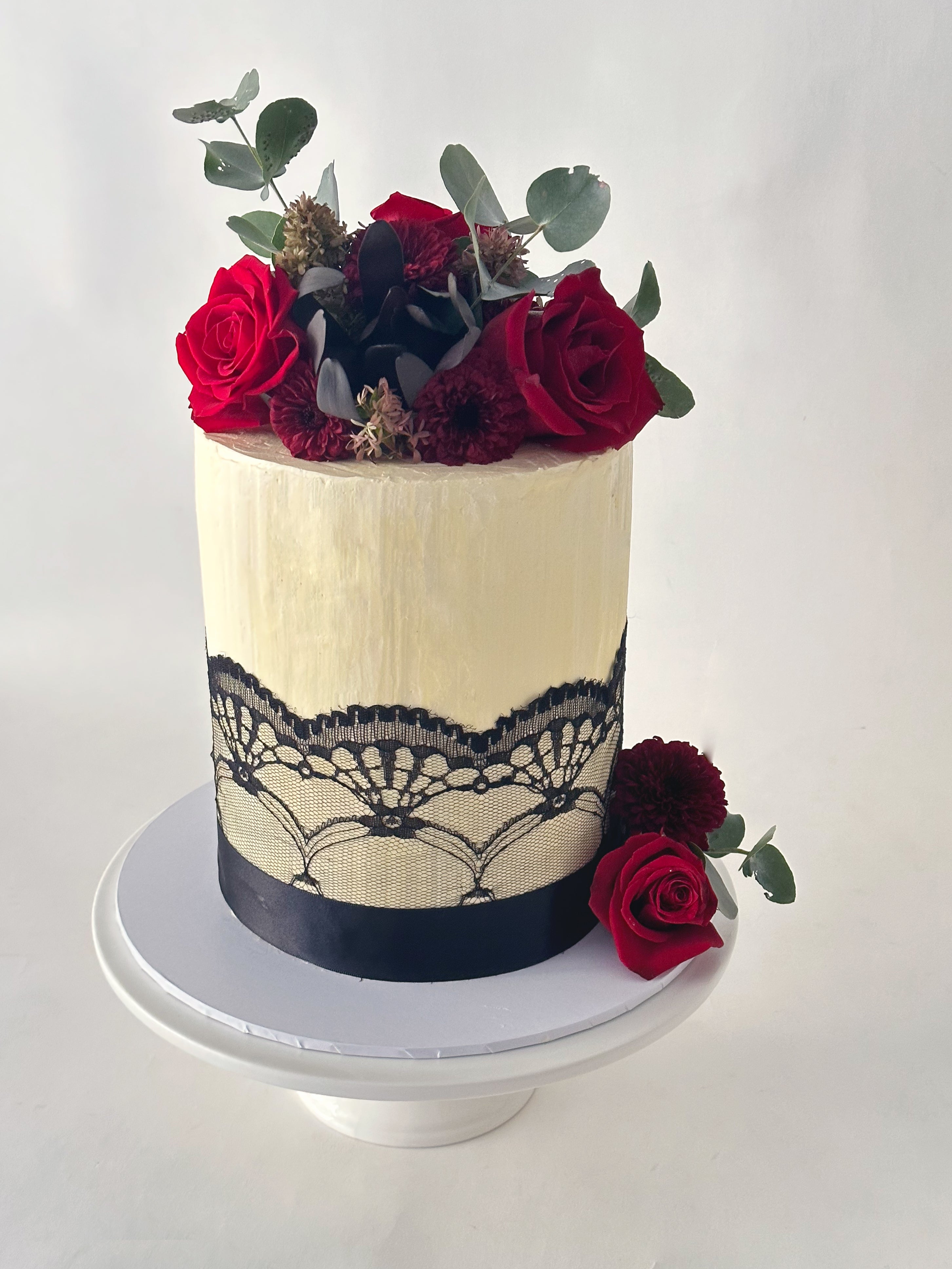 Tall elegant cake decorated with red roses and a black ribbon.